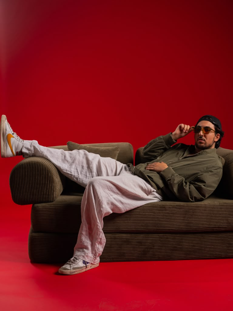 Andrew Aoun lounging on an olive couch against a red backdrop